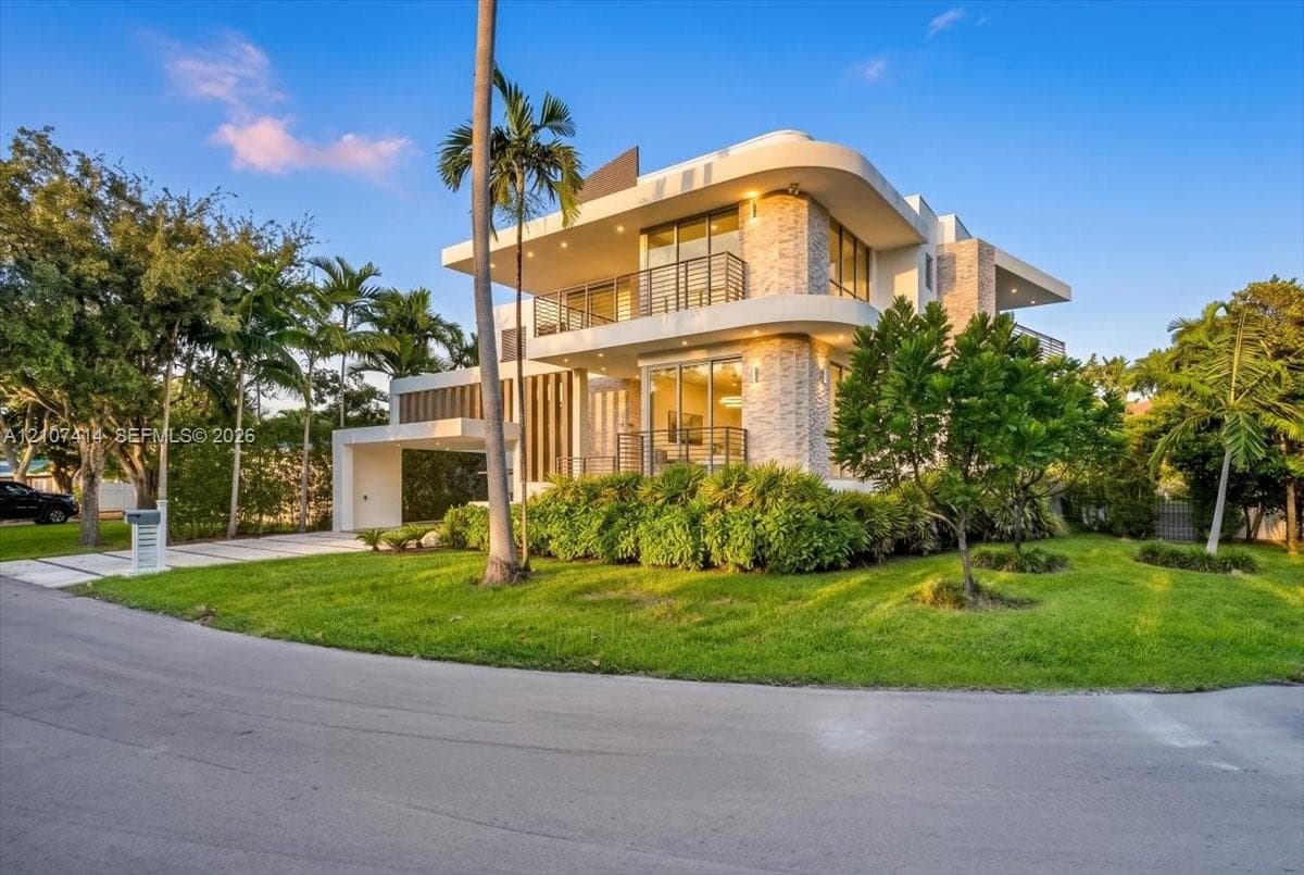 Modern multi-level exterior featuring curved architectural lines, stone-accented facade, expansive glass sliding doors, integrated balcony railings, and a covered porte-cochère