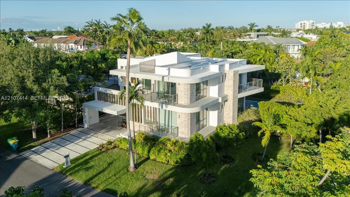 Multi-level modern exterior featuring stone cladding, expansive floor-to-ceiling glass windows, multiple wrap-around balconies, and a concrete paver driveway