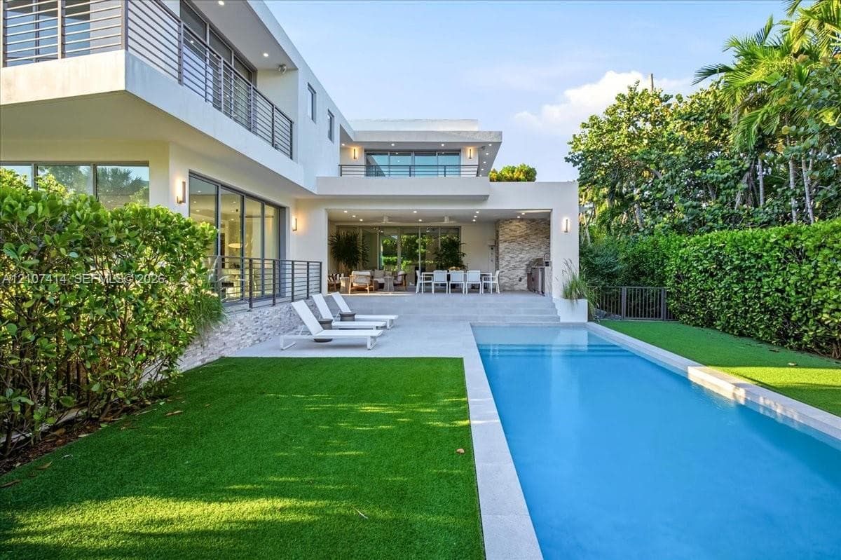 Contemporary multi-level exterior featuring stucco facade, rectangular swimming pool, concrete patio, second-story balconies with horizontal railings, and integrated landscape hedging