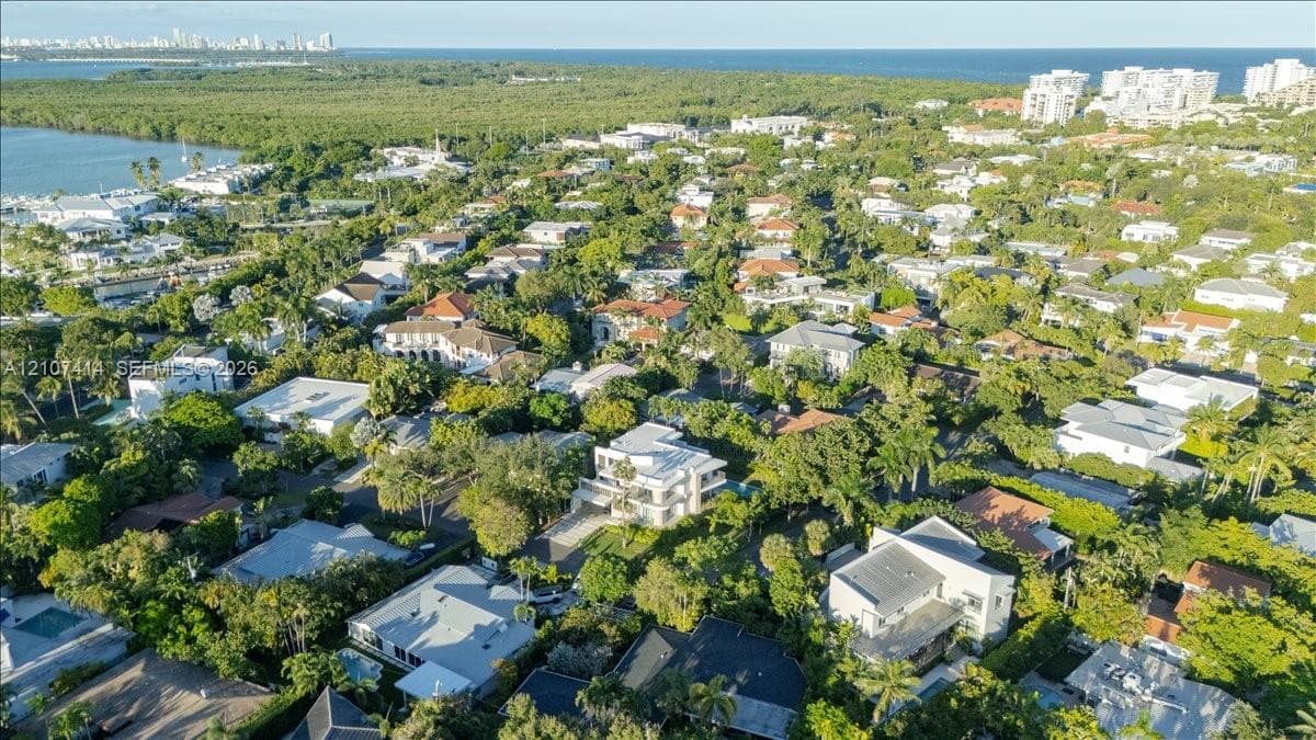 Aerial view showcasing a coastal residential neighborhood featuring mature tree canopy, proximity to the waterfront, and urban skyline backdrop