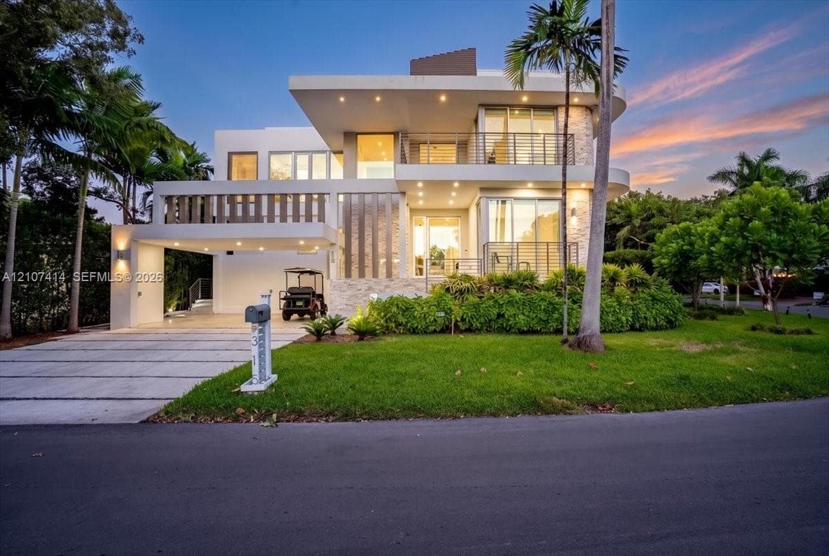 Contemporary multi-level exterior featuring stacked stone accents, integrated recessed lighting, expansive glass balconies with metal railings, and a concrete-paved porte-cochere