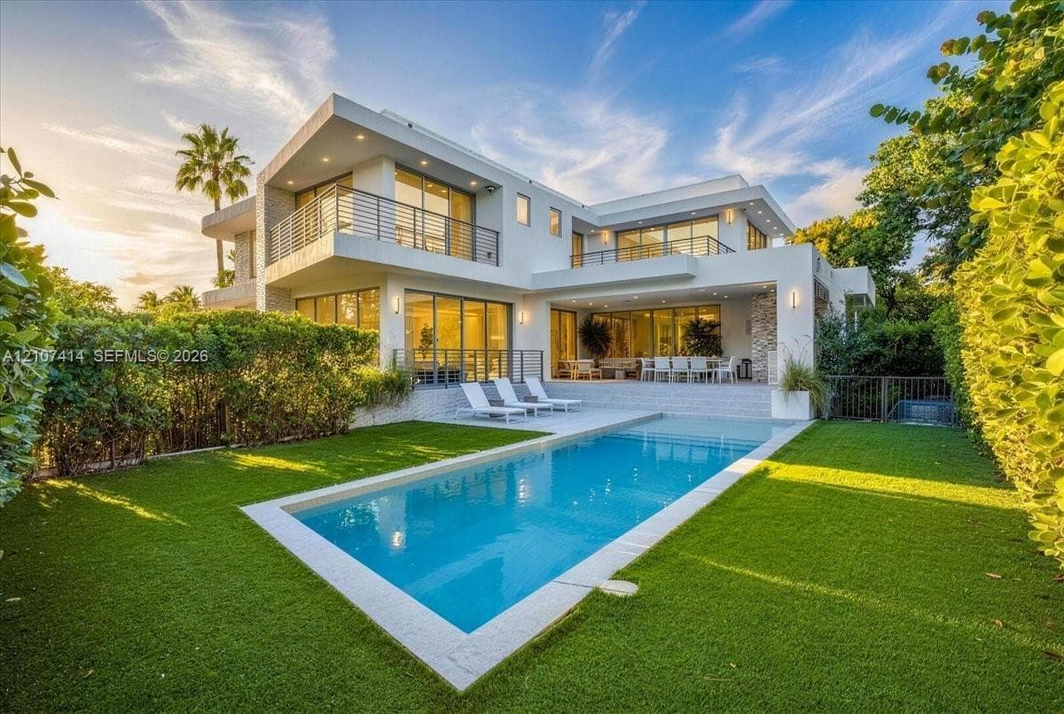 Modern two-story architectural exterior featuring expansive glass sliding doors, multiple balconies with metal railings, a rectangular swimming pool, and stone facade accents