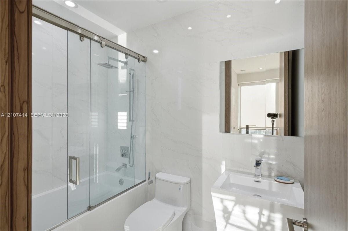 Bathroom featuring full-height stone-finish wall tile, a glass-enclosed shower with a rainfall showerhead, a wall-mounted medicine cabinet, and a contemporary pedestal sink with a chrome faucet