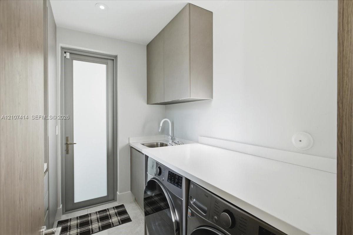 Utility room featuring custom cabinetry, a solid surface countertop, an undermount sink with a high-arch faucet, and a glass-panel door