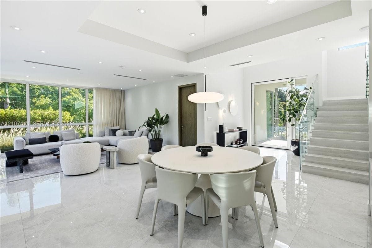 Open-concept interior featuring large-format polished stone flooring, tray ceilings with recessed lighting, floor-to-ceiling windows, and a staircase with a glass-panel railing