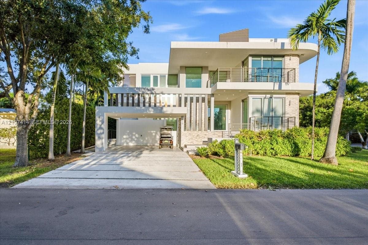 Modern three-story architecture featuring stone masonry accents, a covered parking structure, metal balcony railings, and expansive glass window panels