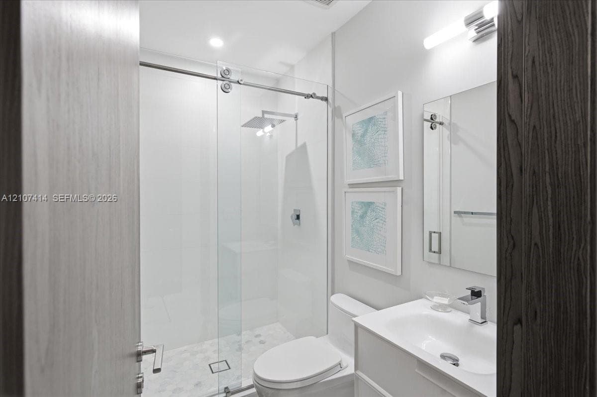 Walk-in shower with sliding glass enclosure and rainfall showerhead, white vanity with integrated basin, polished chrome fixtures, and wall-mounted vanity lighting