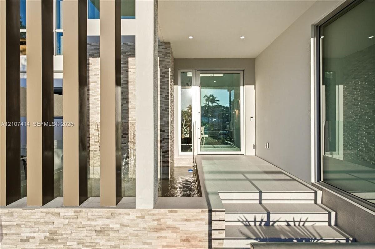 Contemporary entryway featuring vertical architectural screening, tiered stone masonry, recessed ceiling lighting, a water feature, and a glass-paneled entry door