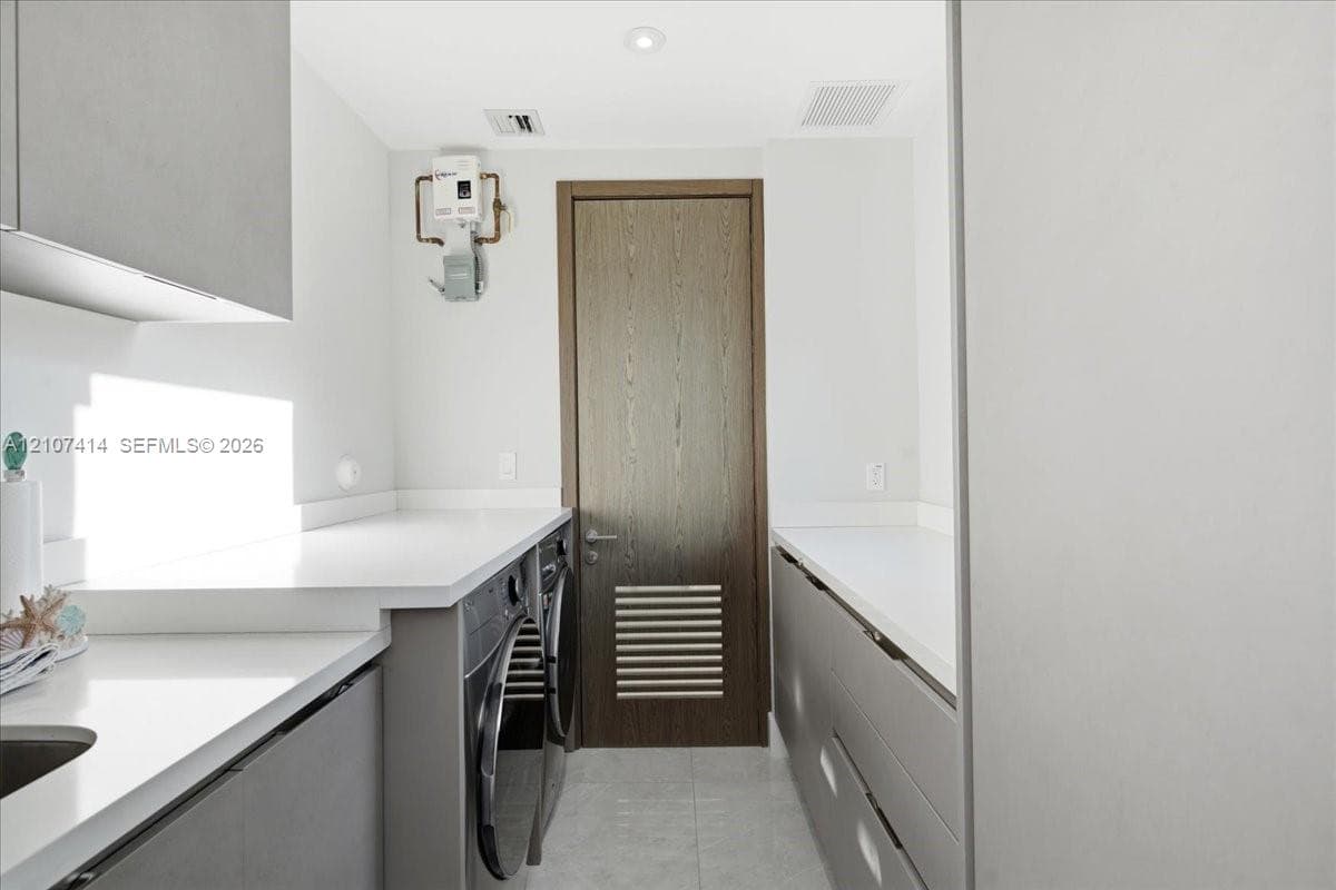 Laundry room featuring grey flat-panel cabinetry, white solid-surface countertops, integrated sink, and wood-finish door with louvered panel