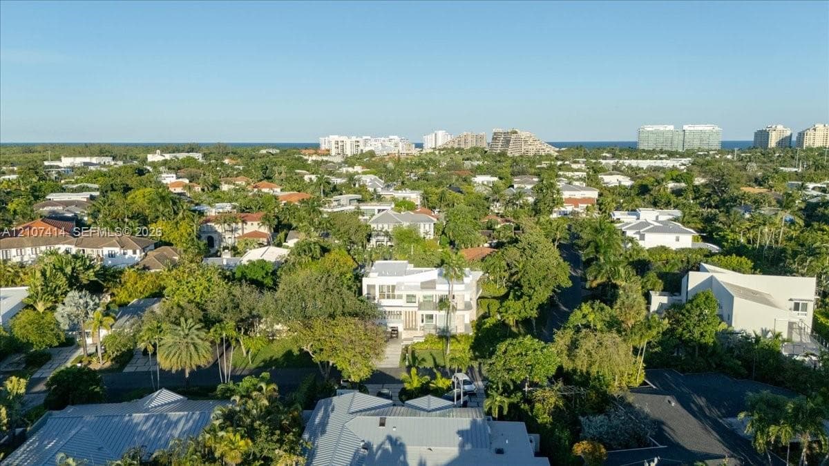 Aerial perspective featuring a multi-level residence with flat rooflines, dense perimeter vegetation, mature canopy trees, and proximity to coastal structures