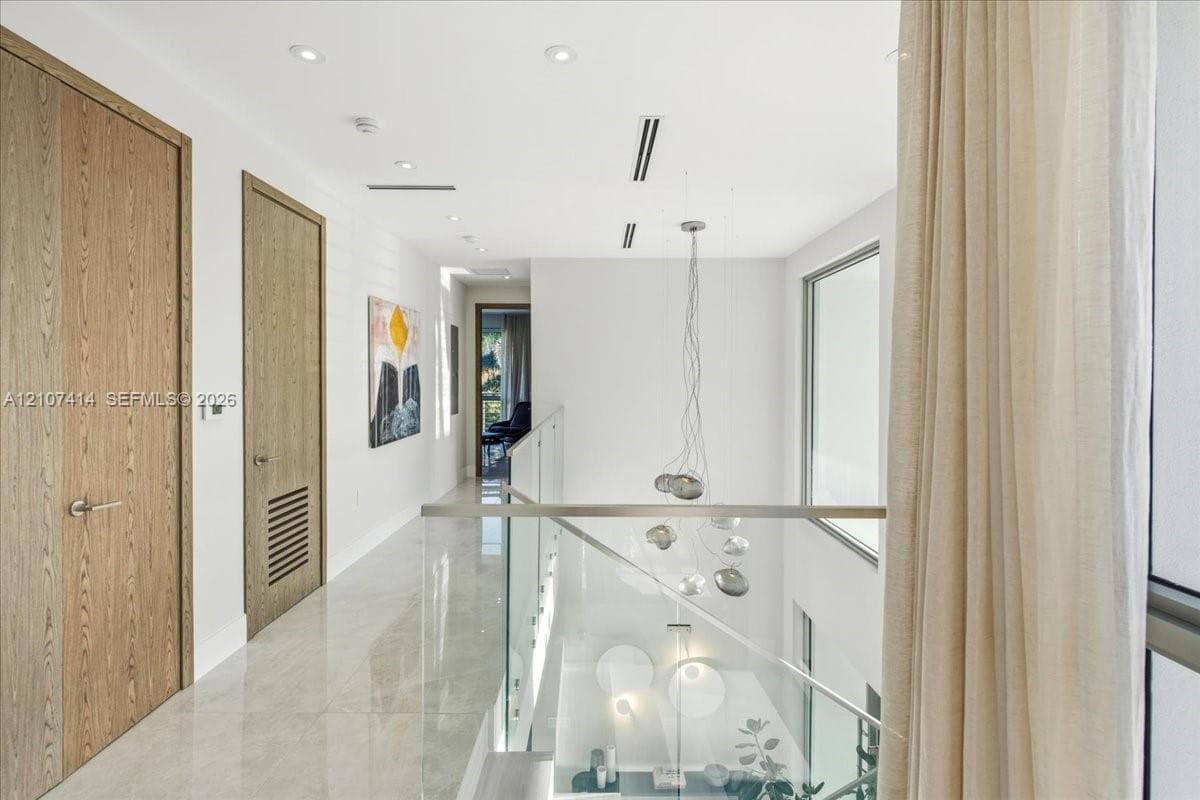 Hallway featuring large-format light tile flooring, wood-finish interior doors, recessed lighting, and a glass panel railing