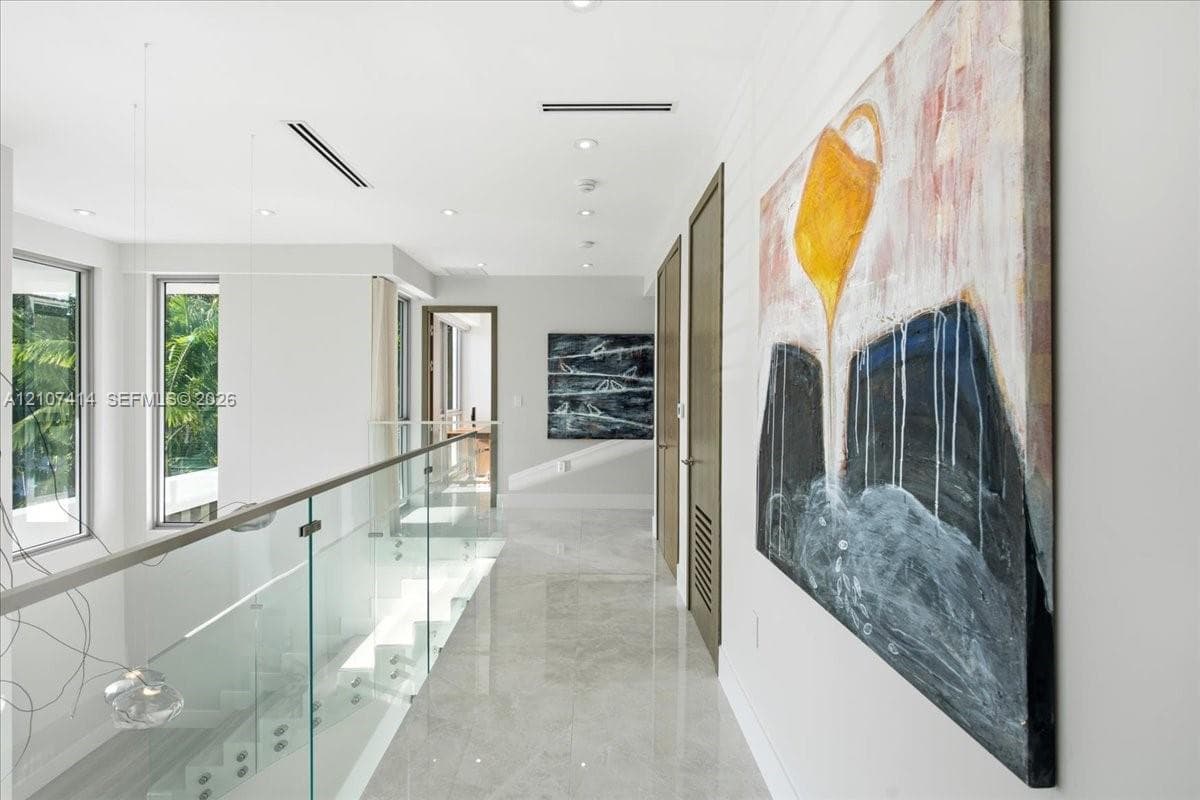 Hallway featuring polished tile flooring, a glass panel railing with metallic hardware, recessed ceiling lighting, and solid wood-finish doors