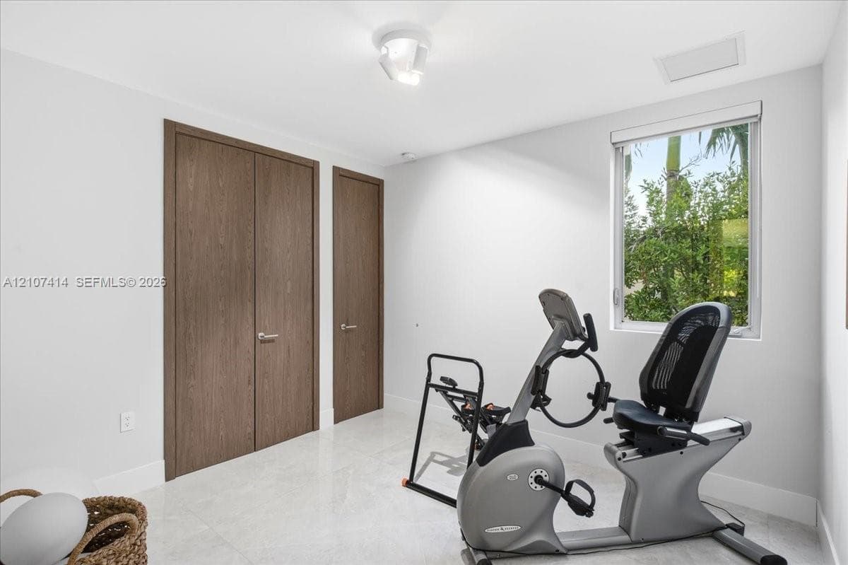 Neutral-toned interior space featuring light-colored stone-finish flooring, solid wood-finish doors with metallic hardware, and a single-pane window with a view of greenery