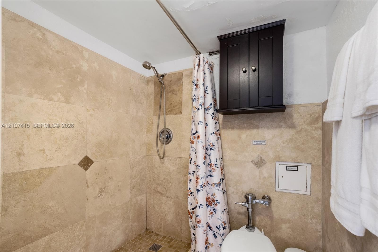 Shower enclosure featuring floor-to-ceiling stone-tile surround, mosaic tile flooring, built-in dark wood-finish cabinetry, and stainless steel hardware