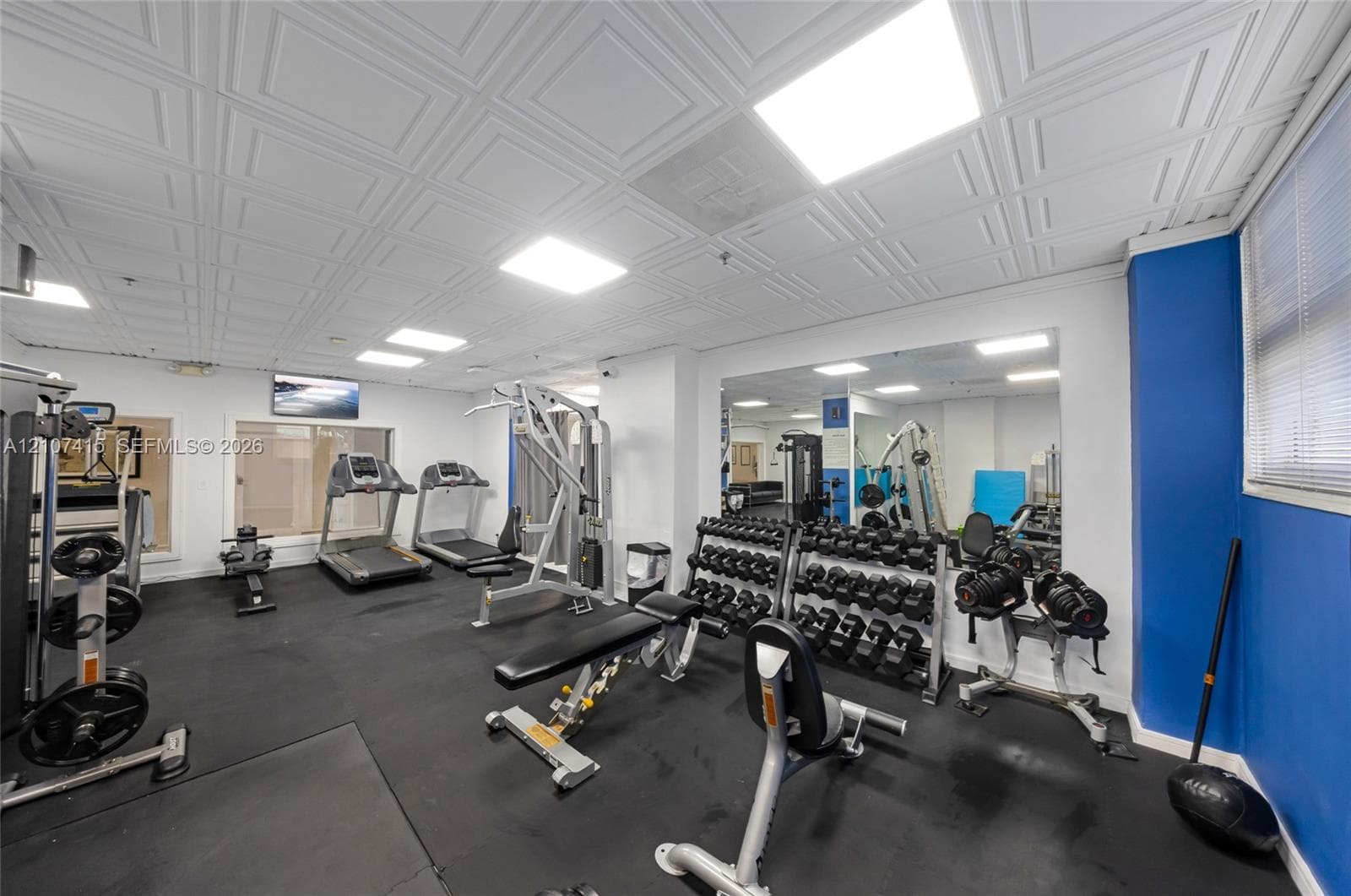 Fitness area featuring a coffered ceiling, recessed lighting, rubberized flooring, and wall-to-wall mirrors