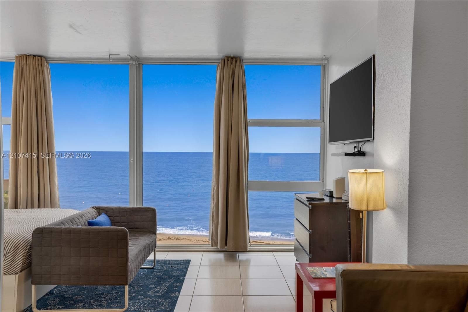 Floor-to-ceiling windows featuring ocean and beach scenery, complemented by light-toned tile flooring