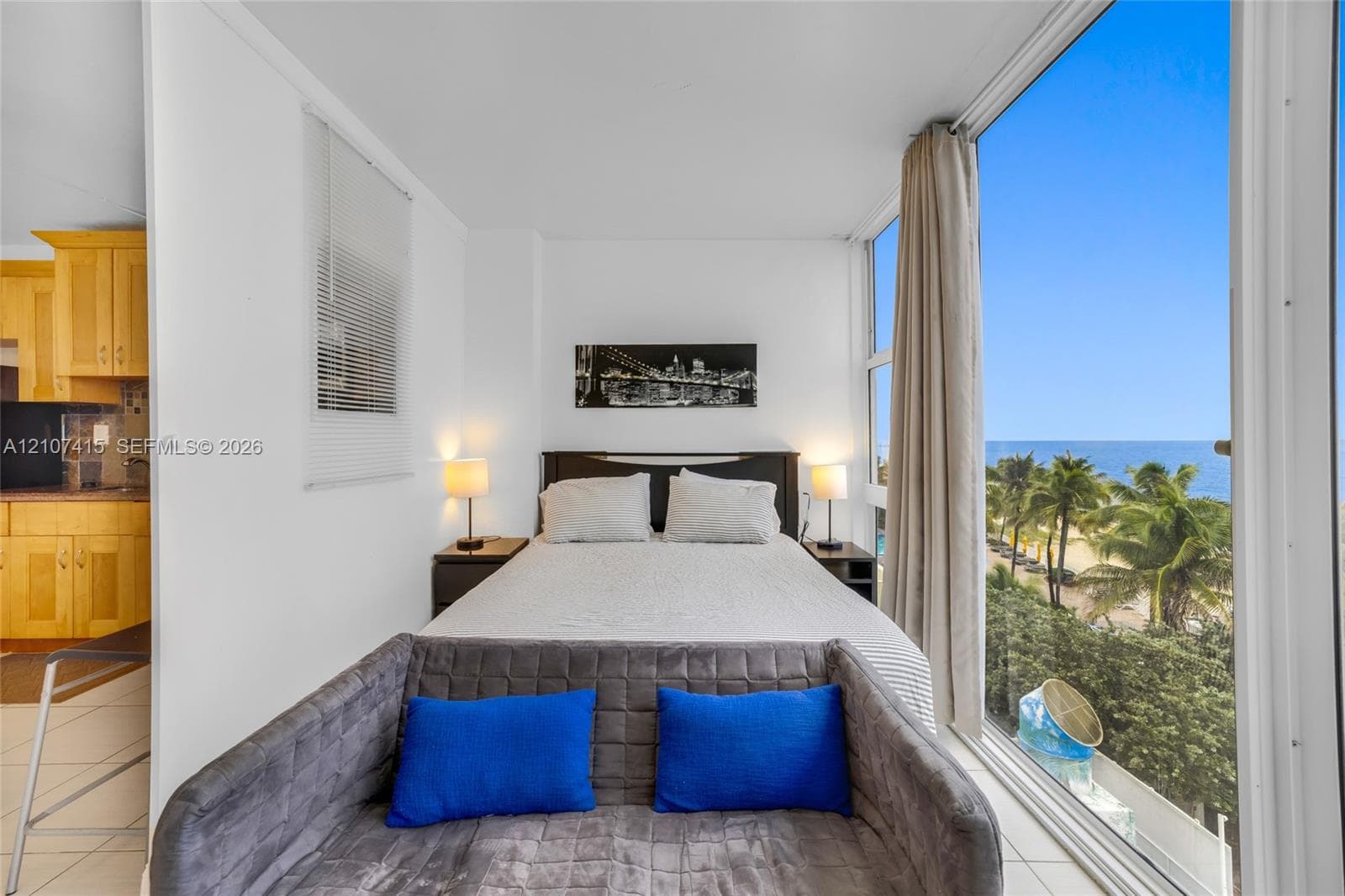 Floor-to-ceiling windows featuring ocean and palm tree scenery, wood cabinetry with horizontal hardware, and light-toned tile flooring