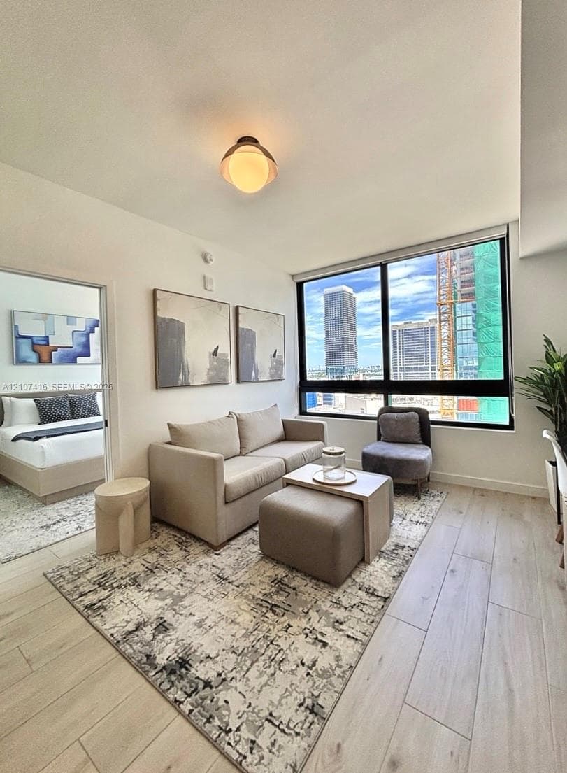 Large floor-to-ceiling windows with urban scenery, wood-finish flooring, and semi-flush mount dome lighting