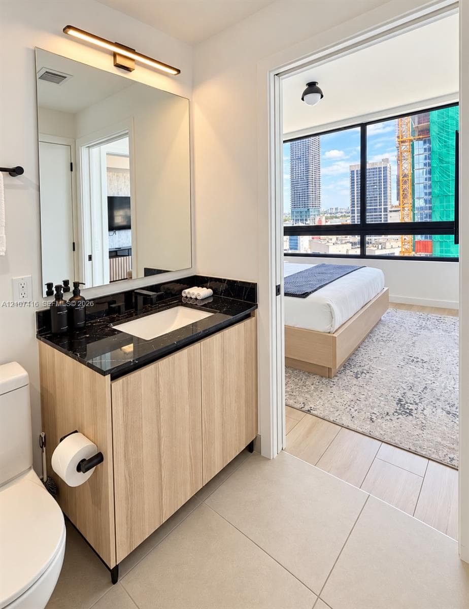 Bathroom vanity featuring a dark stone countertop, an integrated rectangular sink, light wood-finish cabinetry, and a modern wall-mounted light fixture