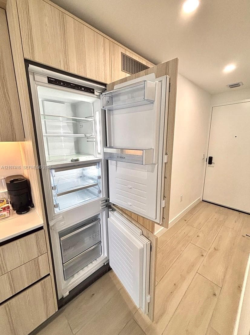Integrated Bosch refrigerator featuring a panel-ready design, light-tone wood-finish cabinetry, white countertop, and wood-finish flooring