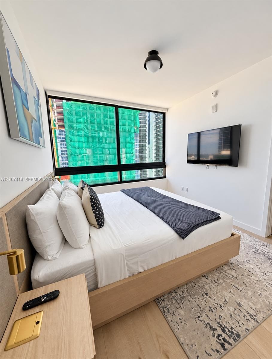 Floor-to-ceiling windows, light-tone wood-finish flooring, and a flush-mount overhead light fixture