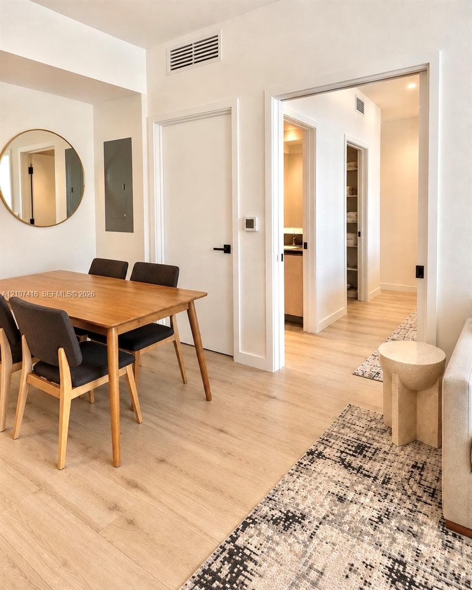 Light-toned wood-finish flooring, crisp white interior doors with matte black hardware, and a circular wall-mounted mirror