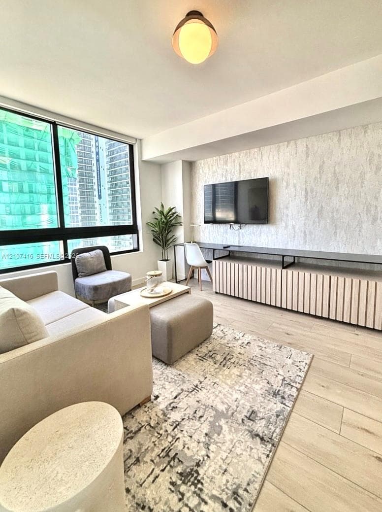 Floor-to-ceiling windows, integrated slatted cabinetry, textured accent wall, wood-finish flooring, and minimalist ceiling-mounted light fixture