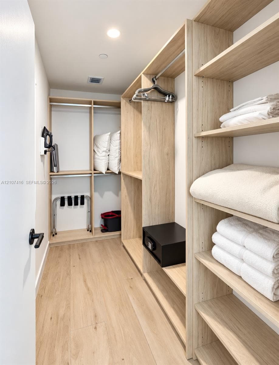 Walk-in closet featuring light wood-finish shelving, multiple hanging rods, and integrated floor-to-ceiling storage units