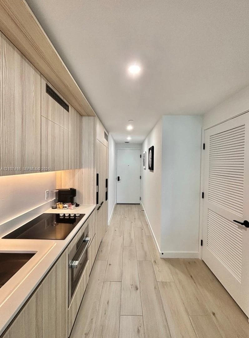 Kitchen featuring wood-finish cabinetry, light-toned wood-finish flooring, recessed lighting, integrated appliances, and louvered-style door