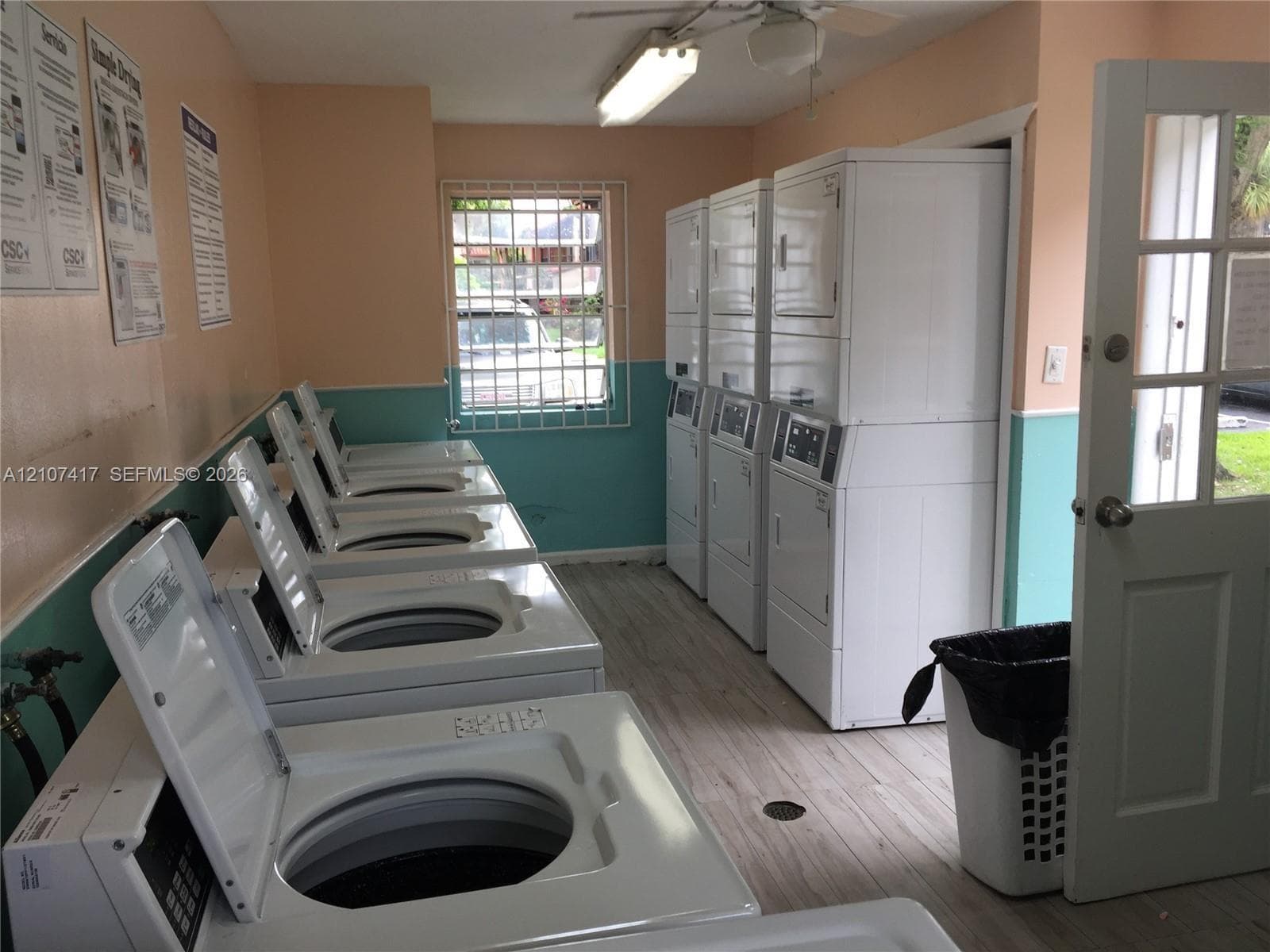 Laundry facility featuring multiple top-loading washing machines, stackable laundry units, wood-finish flooring, and a multi-pane glass door