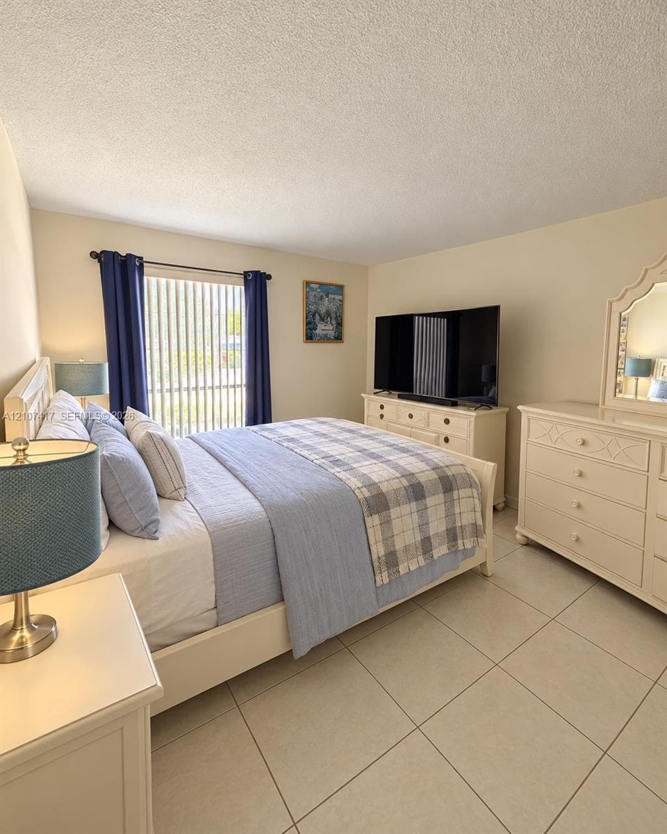 Neutral-toned ceramic tile flooring, textured ceiling, and large sliding glass door with vertical blinds