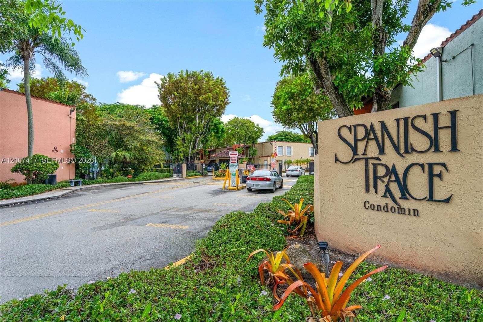 Community entrance featuring a gated access point, mature landscaping, and stucco signage