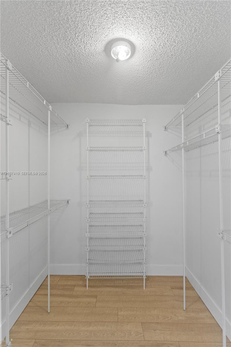 Walk-in closet featuring white wire shelving units and wood-finish flooring