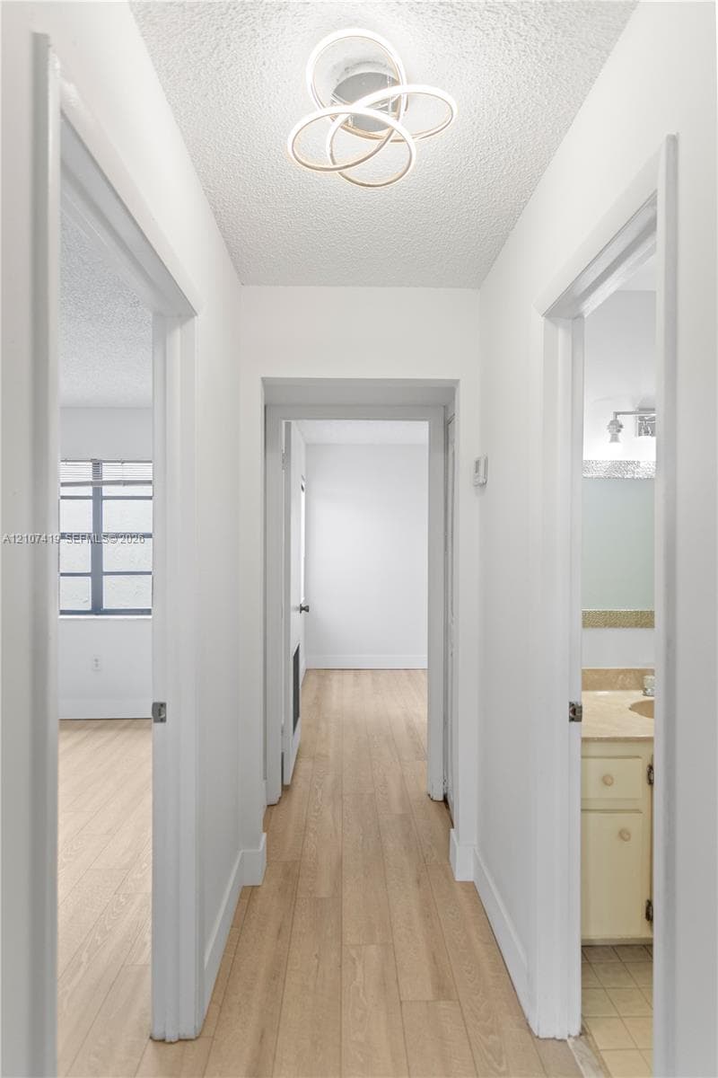 Hallway featuring wood-finish flooring, textured ceiling, contemporary circular flush-mount light fixture, and door-entry access to multiple rooms