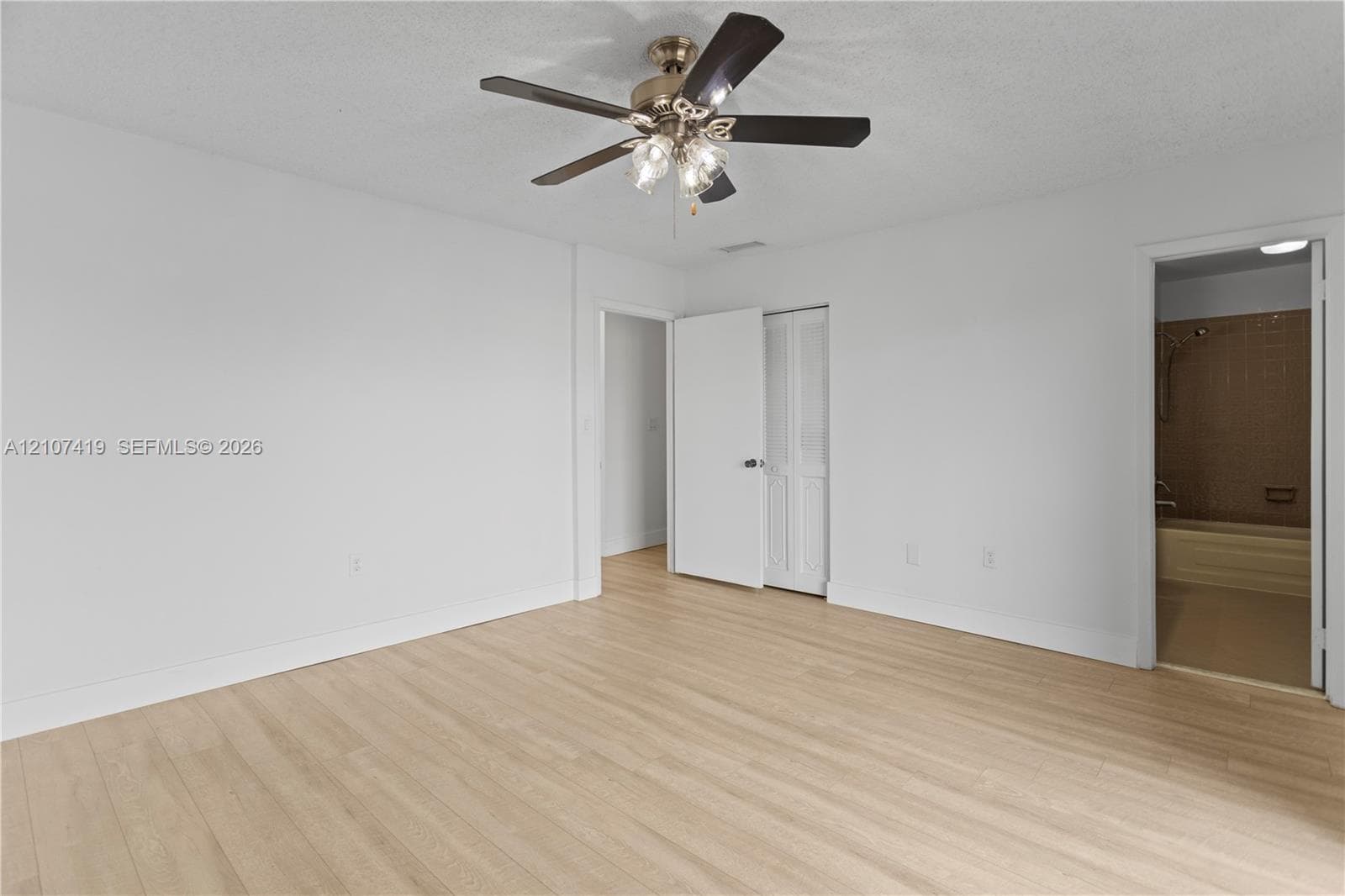 Interior space featuring light-toned wood-finish flooring, a multi-blade ceiling fan with integrated light fixture, and bifold closet doors