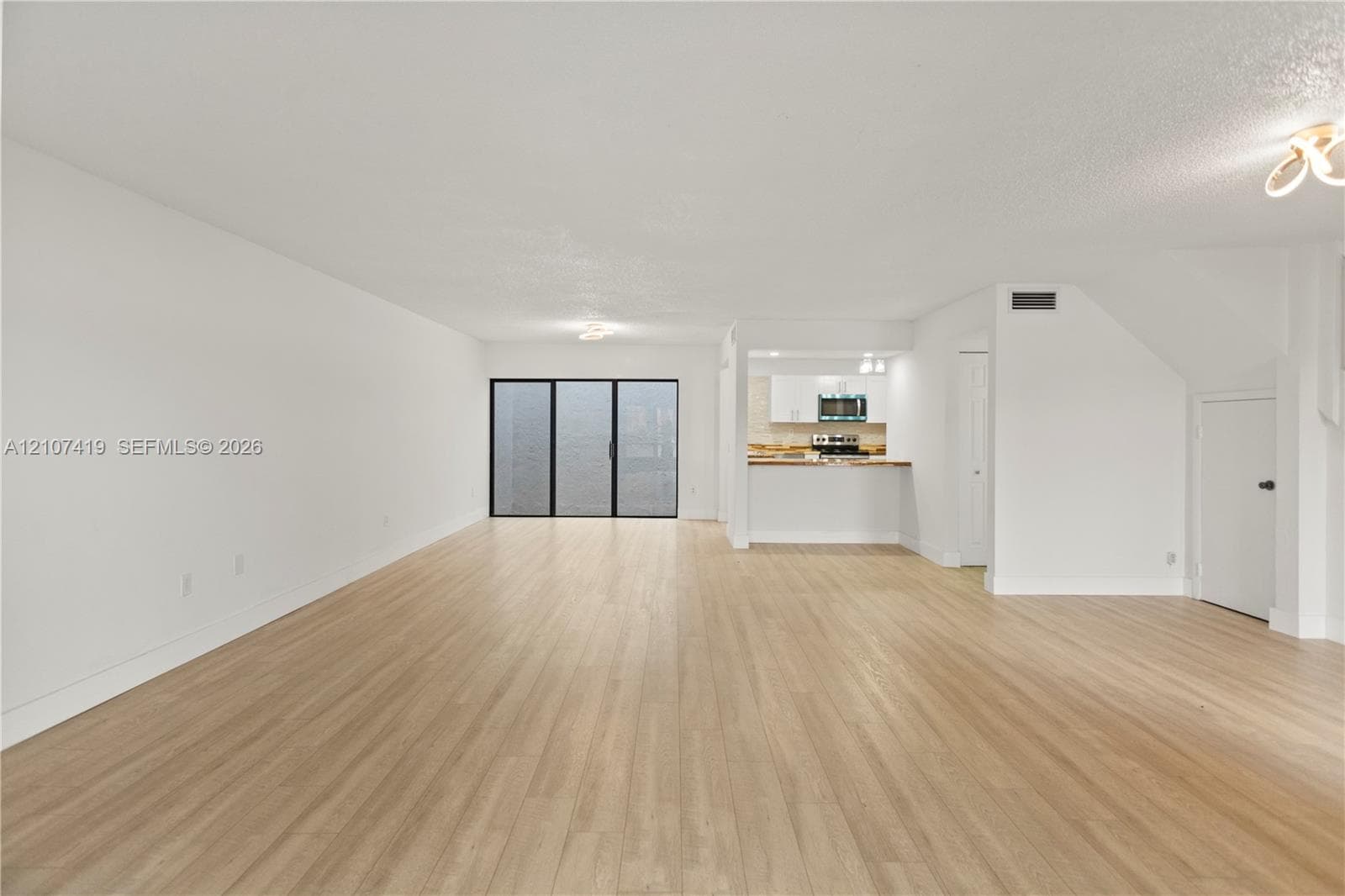 Open-concept interior featuring light-tone wood-finish flooring, white cabinetry, a kitchen pass-through counter, and a glass sliding door system