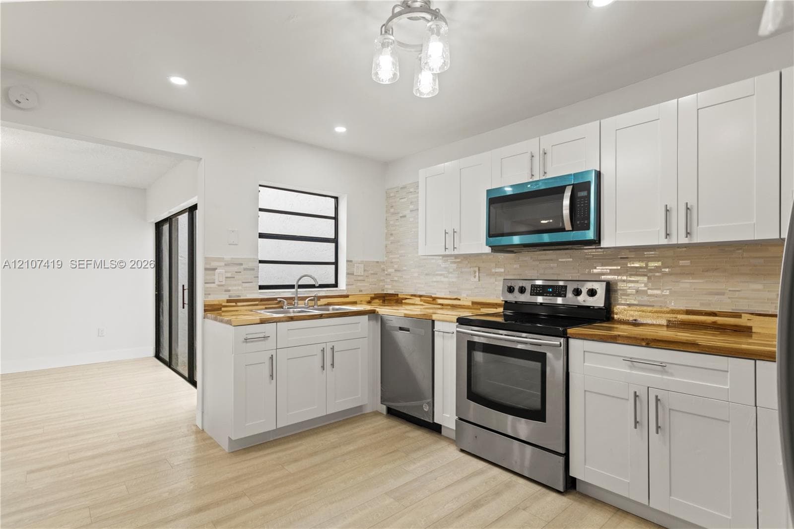 Kitchen featuring white Shaker-style cabinetry, wood-finish countertops, stainless steel appliances, a multi-tone mosaic tile backsplash, and recessed lighting