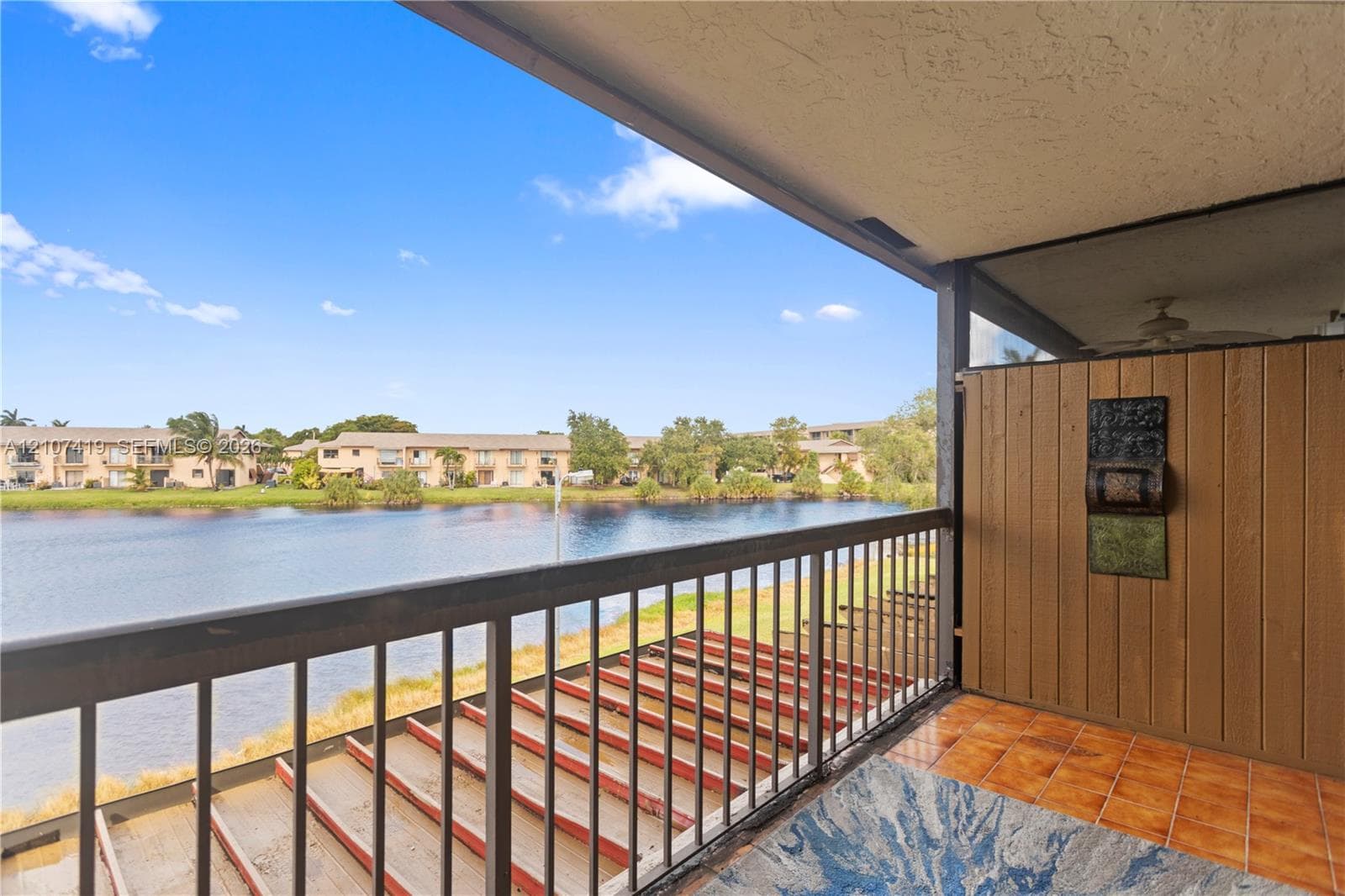 Covered balcony featuring tile flooring, vertical wood-finish paneling, and a metal railing overlooking the water