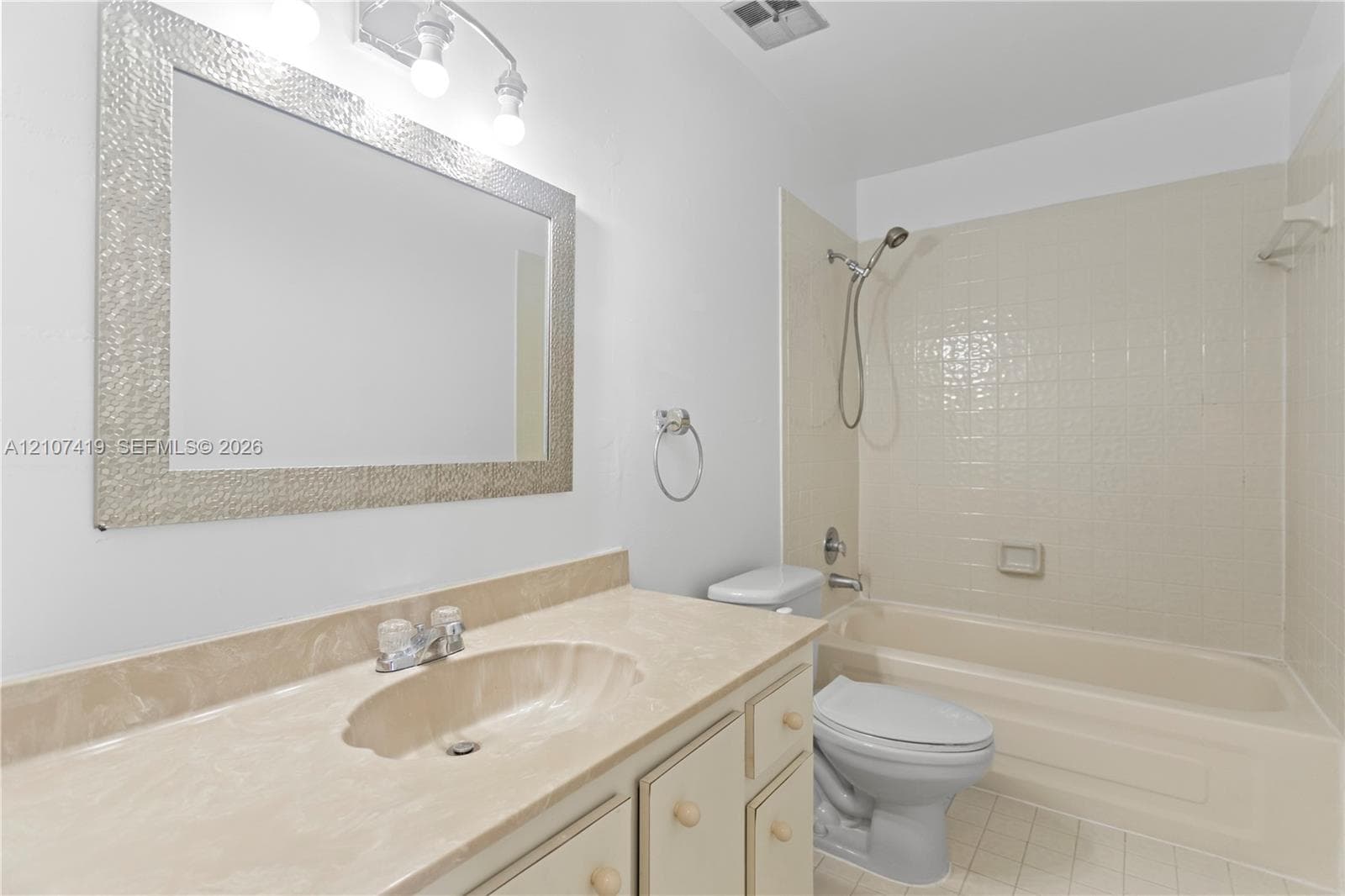Bathroom featuring an integrated vanity countertop with a recessed basin, a framed wall mirror, a three-light fixture, and a tub-shower combination with tile surround