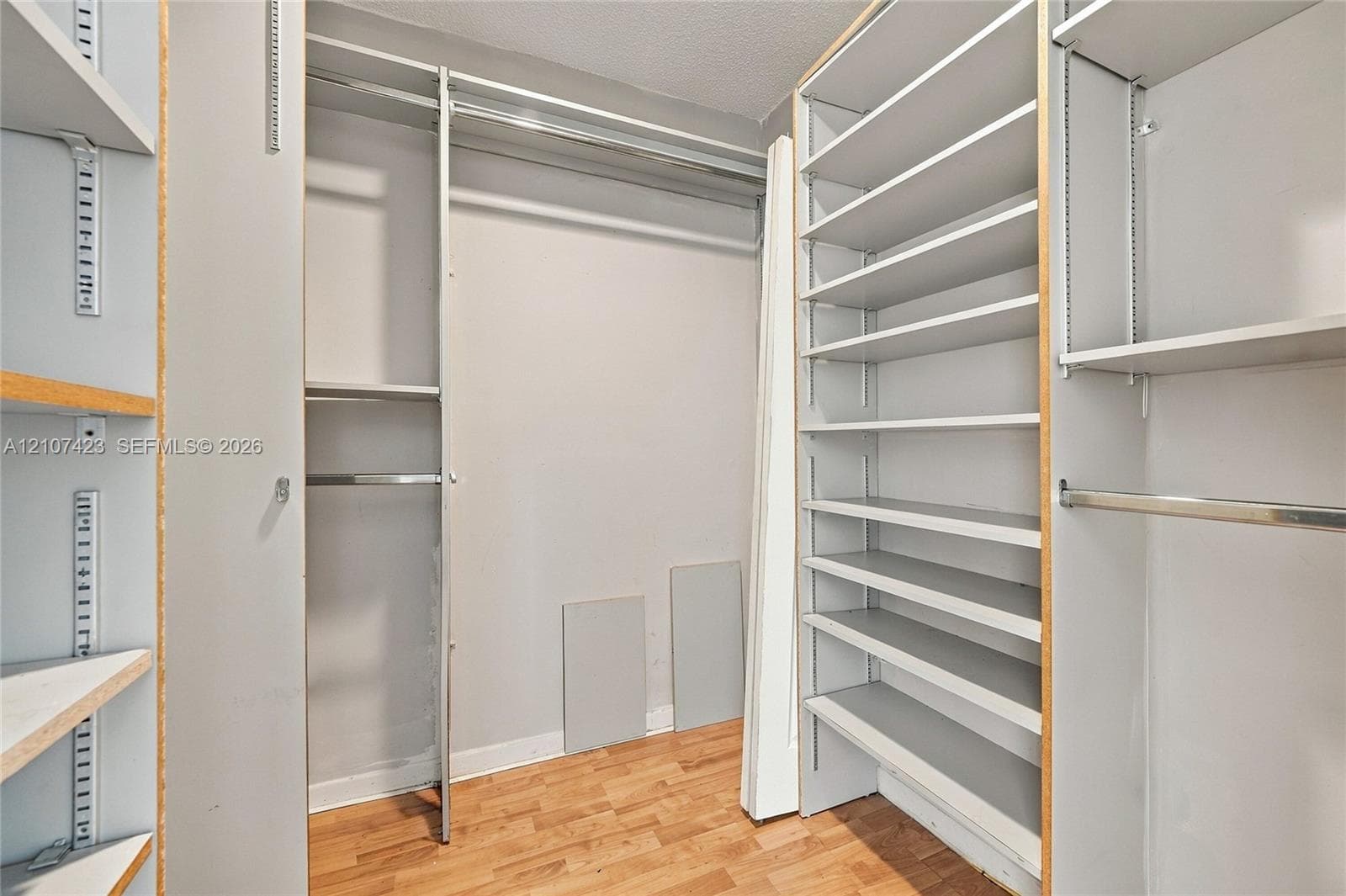 Storage area featuring adjustable shelving units, metal hanging rods, and wood-finish flooring