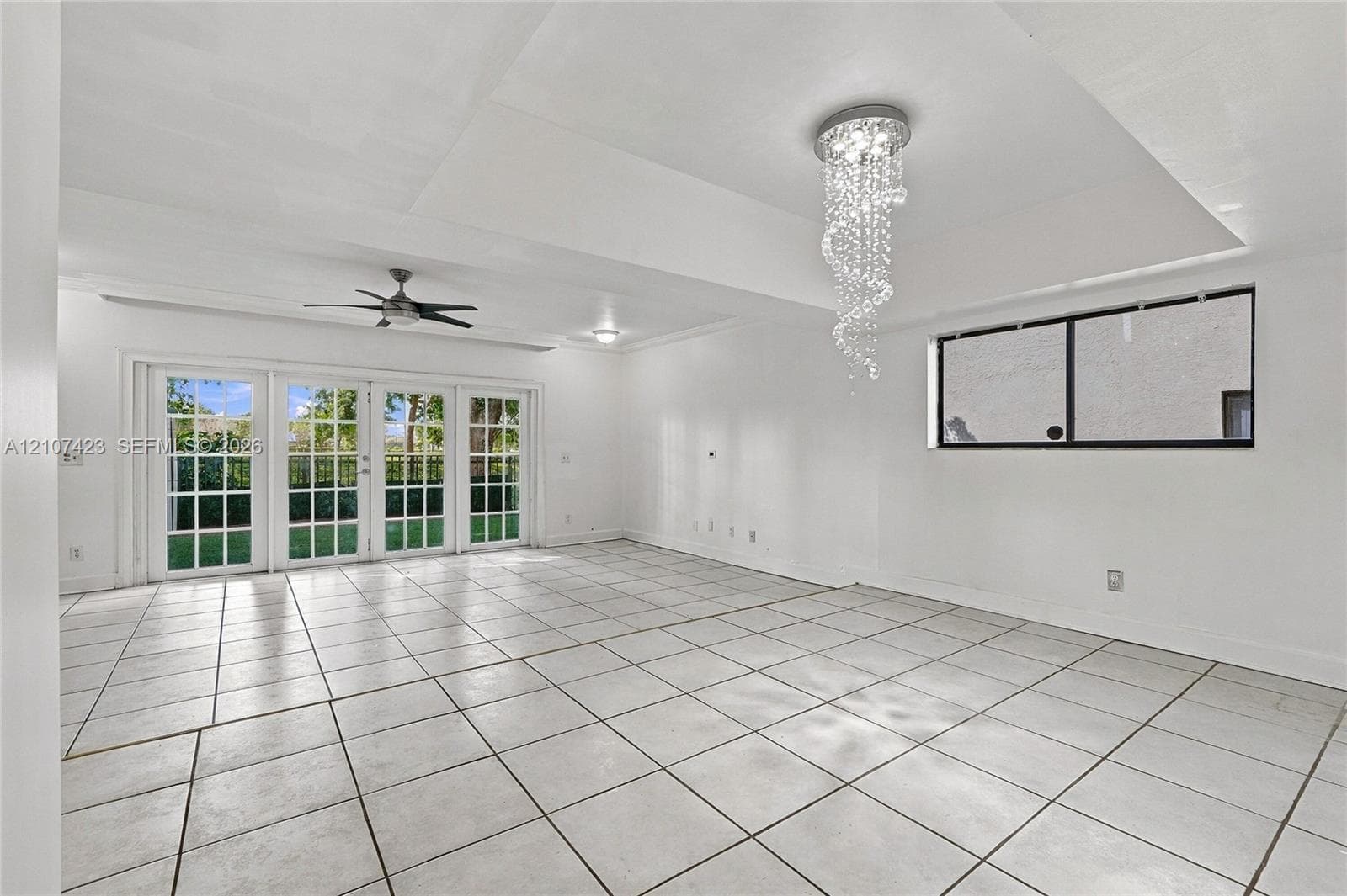 Interior space featuring tile flooring, a tray ceiling, crystal chandelier, ceiling fan, and multipane French doors