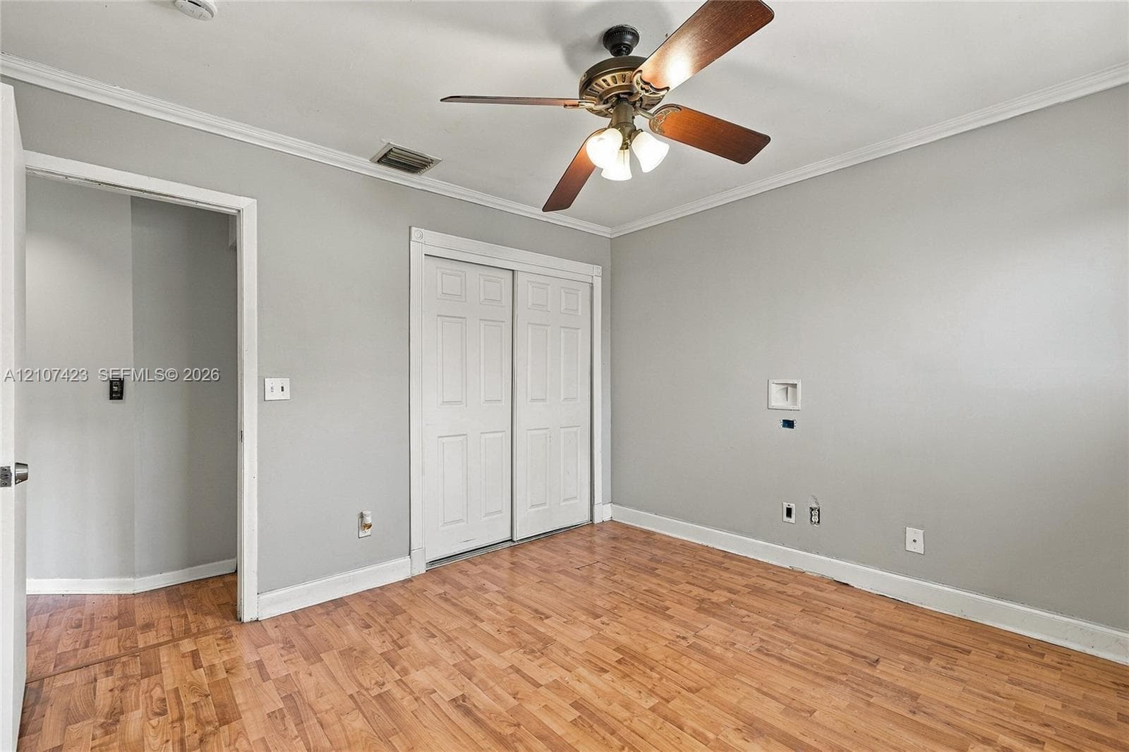Interior space featuring wood-finish flooring, crown molding, a central ceiling fan with integrated lighting, and a double-panel closet door