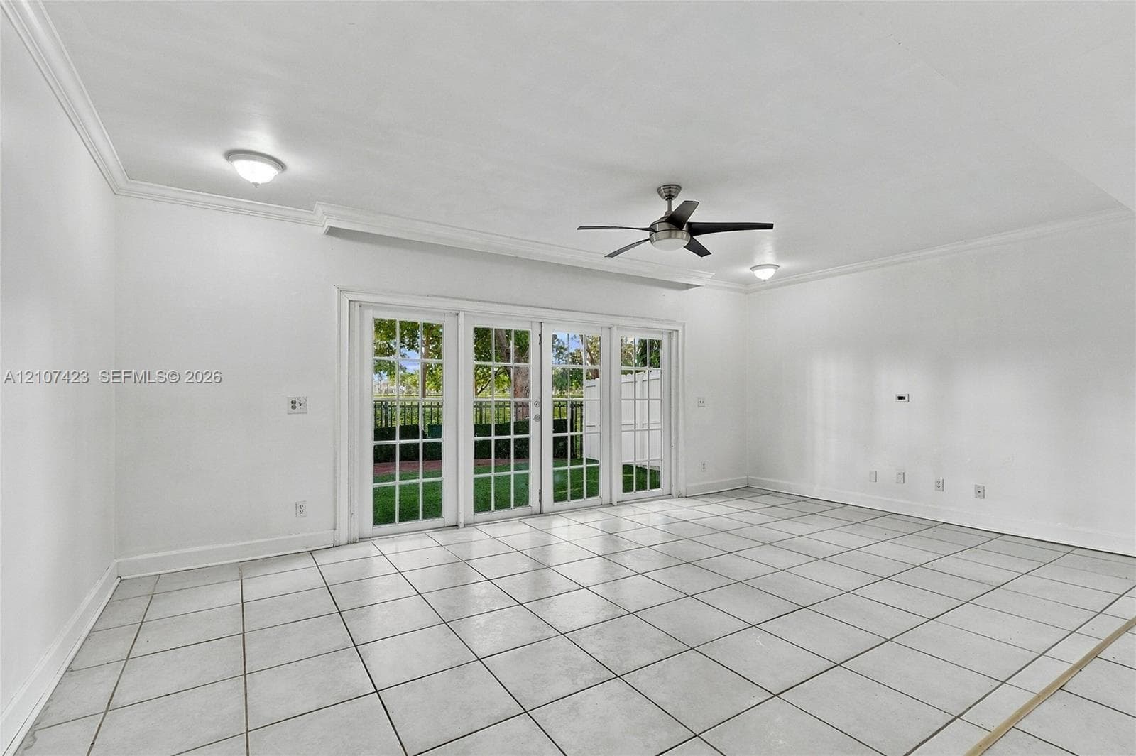 Interior space featuring large-format tile flooring, crown molding, multi-panel glass patio doors, and a ceiling fan