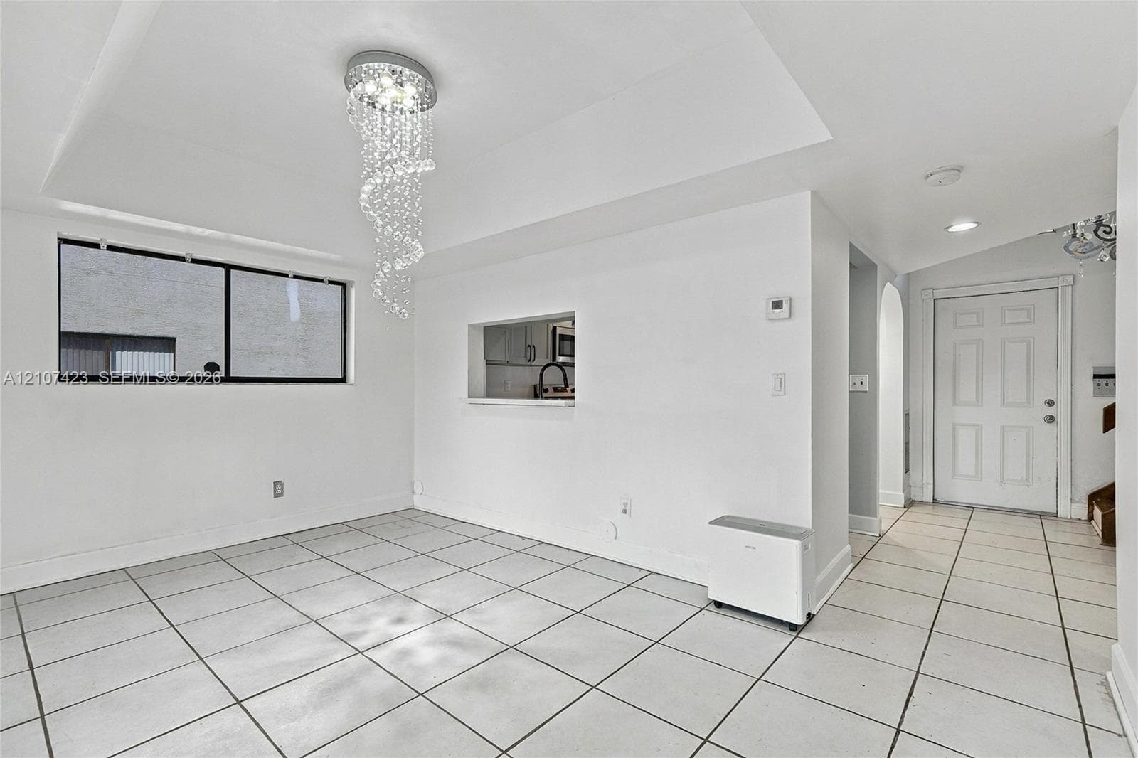 Open interior space featuring large-format ceramic tile flooring, a recessed ceiling with a crystal drop chandelier, and a cut-out wall opening