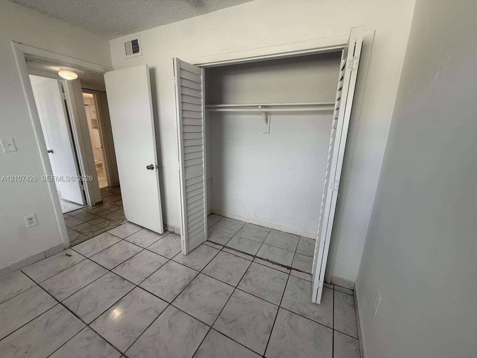 Interior space featuring white-tiled flooring and a closet with white louvered doors