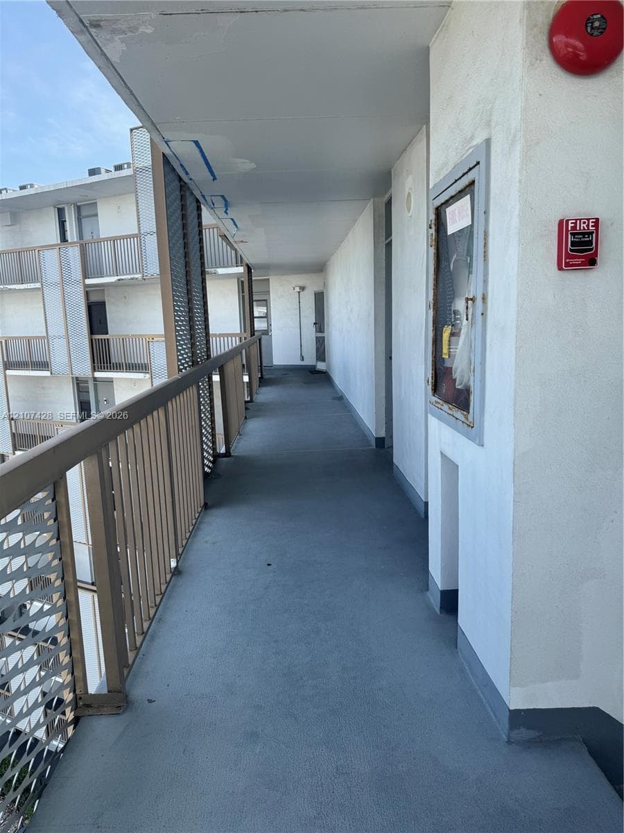 Covered exterior walkway featuring a protective metal railing, textured stucco walls, and a recessed fire safety cabinet