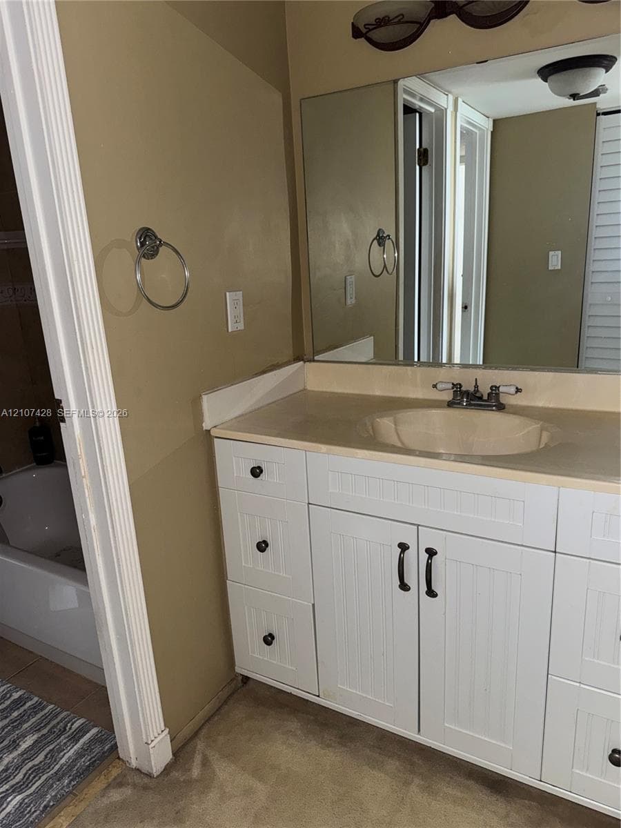 White vanity with beadboard-style cabinetry, solid-surface countertop, integrated basin, chrome dual-handle faucet, and oversized wall-mounted mirror