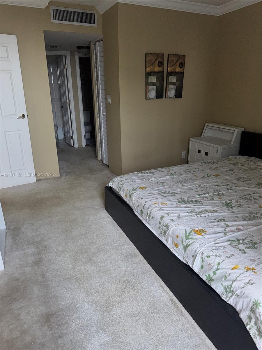 Room featuring neutral-toned walls, carpeting, crown molding, and louvered closet doors