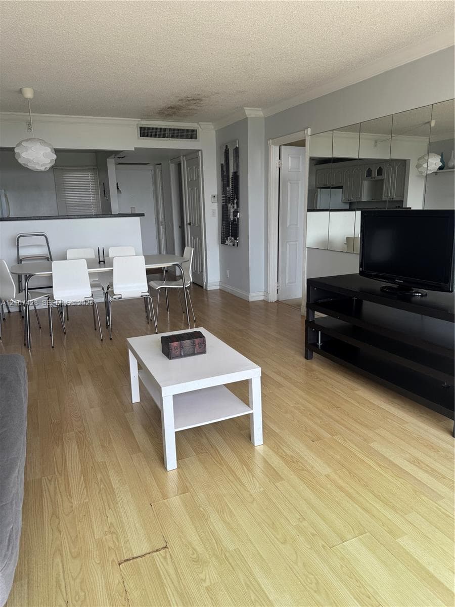 Open-concept interior featuring light wood-finish flooring, a mirrored wall accent, and a built-in kitchen pass-through counter