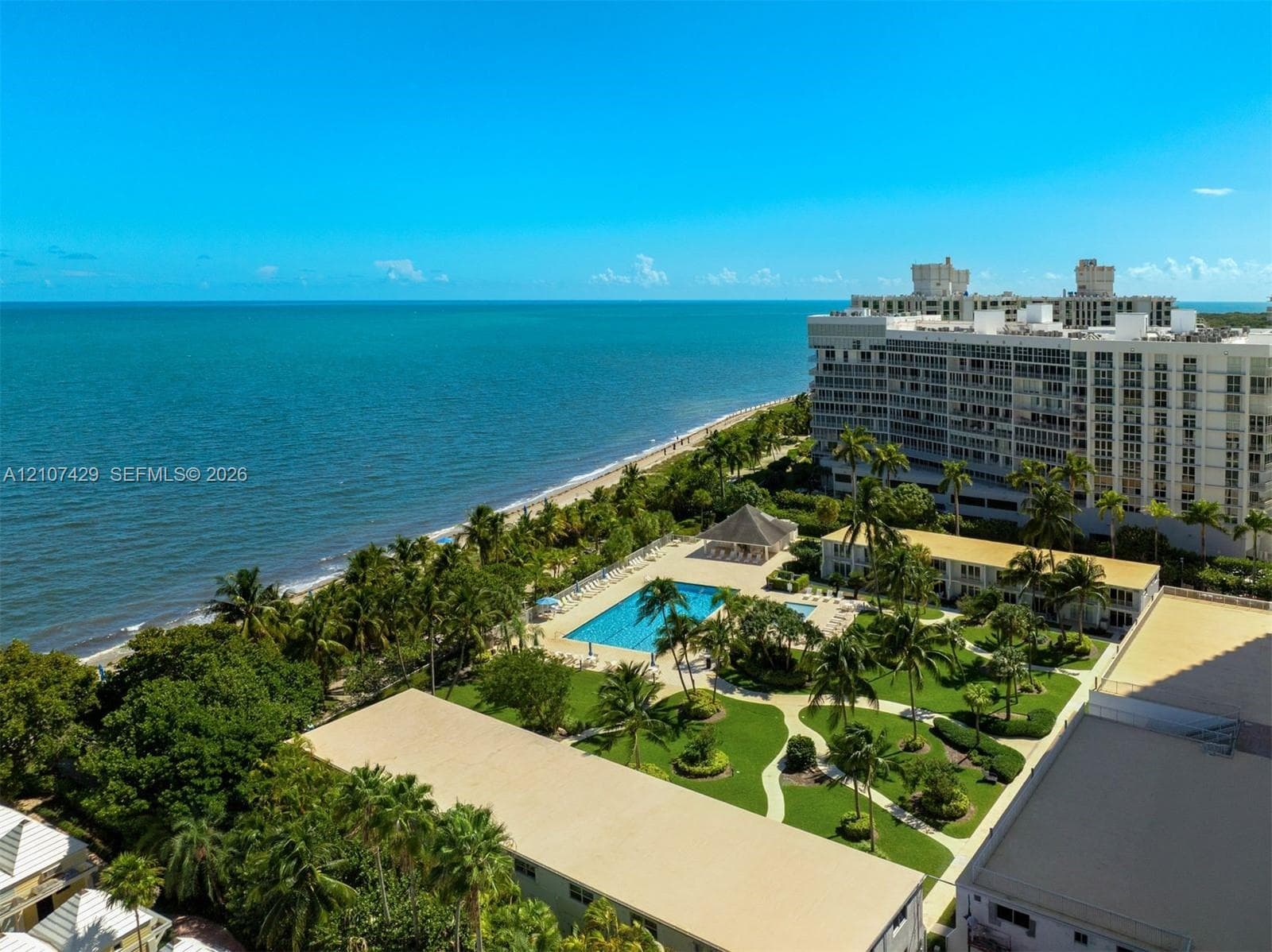 Sandy path featuring a wooden boardwalk, metal railings with rope accents, mature palm trees, and coastal water access